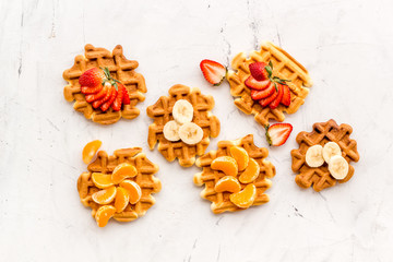 Fototapeta premium Homemade Viennese waffles with strawberry, tangerine and banana topings on white background top view