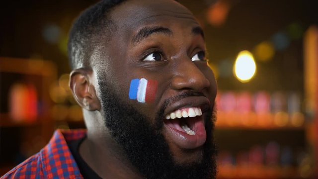 Very emotional black fan with french flag painted on cheek cheering for team