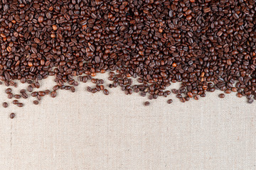 Roasted coffee beans on linea canvas with space on the bottom.
