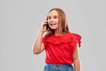 childhood and people concept - beautiful smiling girl in red shirt and skirt calling on smartphone over grey background