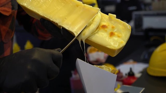 Scraping melted traditional Swiss Raclette cheese. Chef in black gloves scrapes cheese with a knife. Swiss cheese. Cooking