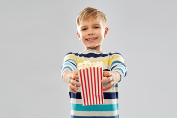 Fototapeta premium fast food, unhealthy eating and childhood concept - little boy in striped pullover holding popcorn from paper bucket over grey background