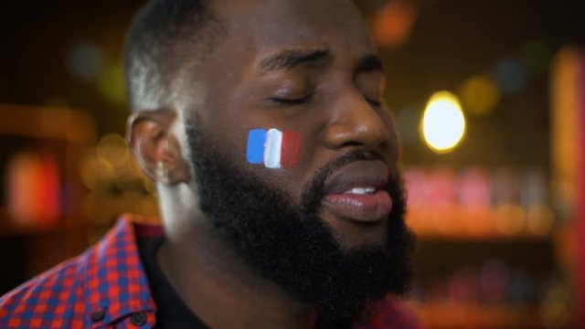 Black french football supporter with flag on cheek unhappy with team failure