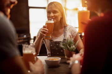 Happy woman drinking beer while spending time with friends in a bar.