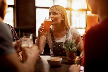 Young woman drinking  beer with her friends in a pub.
