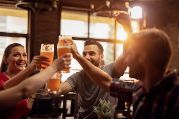 Group of cheerful friends toasting with beer in a bar. - obrazy, fototapety, plakaty