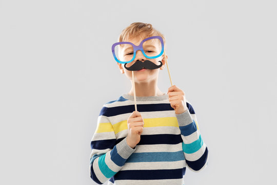 party props, photo booth and childhood concept - little boy with glasses and black vintage moustaches over grey background