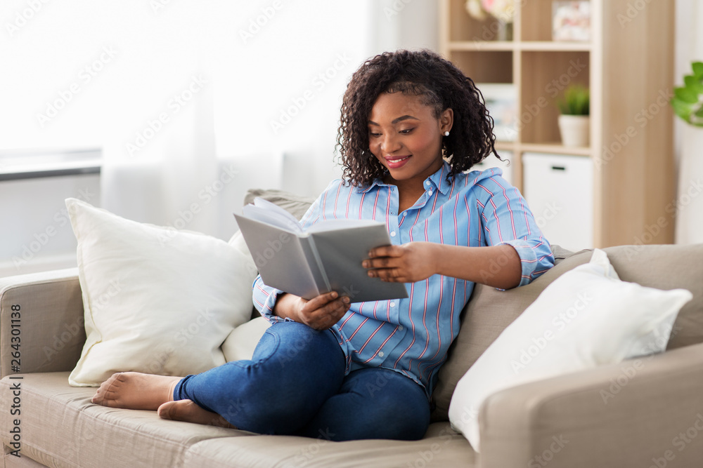 Wall mural leisure, literature and people concept - smiling african american woman reading book at home - Wall murals