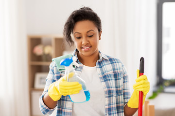 cleaning, housework and housekeeping concept - african american woman or housewife with mop and detergent sprayer at home