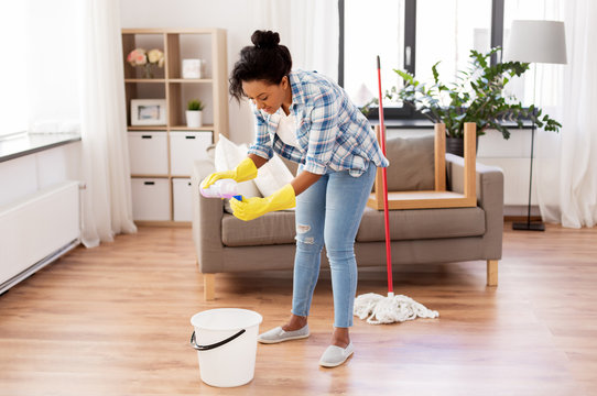 people, housework and housekeeping concept - african american woman or housewife with bucket and mop adding floor cleaning detergent to bottle cap at home
