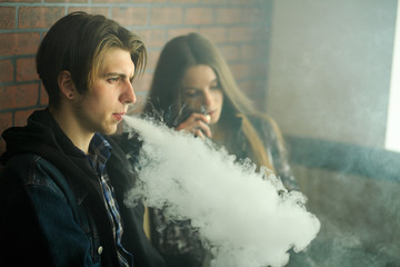 Vape teenagers. Young cute girl in sunglasses and young handsome guy smoke an electronic cigarettes...