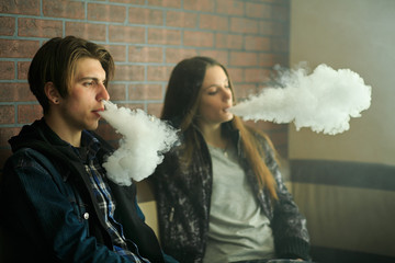 Vape teenagers. Young cute girl in sunglasses and young handsome guy smoke an electronic cigarettes...