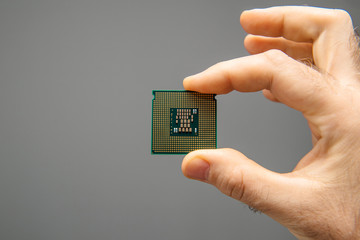 Male hand holding new powerful CPU Central processing unit with high core count and elevated frequency - isolated on gray office background