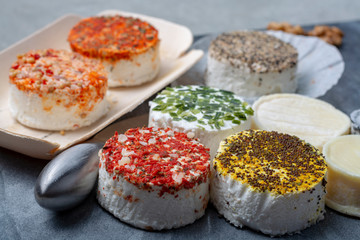 Assortment of French fresh white soft goat cheeses with different tastes topping made with herbs, paprika, indian curry, bruscetta, chives and dried tomatoes