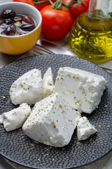 Fresh young soft white Feta cheese on black plate seasoned with dried oregano herb