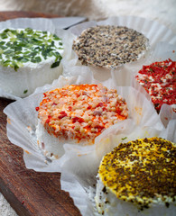 Assortment of French fresh white soft goat cheeses with different tastes topping made with herbs, paprika, indian curry, bruscetta, chives and dried tomatoes