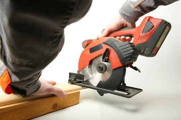 portable circular saw in the hands of a worker is sawing a wooden Board on a white background. man's hands saw off the Board by a accumulator circular saw on a white background - obrazy, fototapety, plakaty