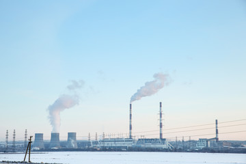 power plant in winter at sunset. large hydroelectric power station on the horizon. smoking smokestacks thermal power plant on the background of the blue sky