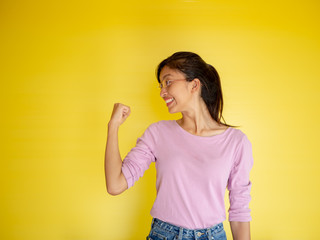 Happy successful young woman with raised hands shouting and celebrating success over yellow background