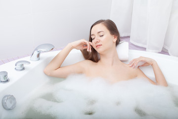 Obraz na płótnie Canvas Young pretty woman relaxes in bathtub with soap foam. Spa procedures in bathroom at home or hotelroom. Skin care and moisturizing for youth preservation.