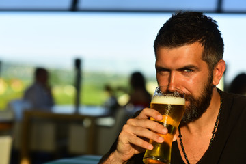 Hipster relaxing at pub. Cheerful young man holding glass of beer and looking at camera.