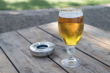 Cold Beer Glass with Metal Ashtray ontop of Wooden Table