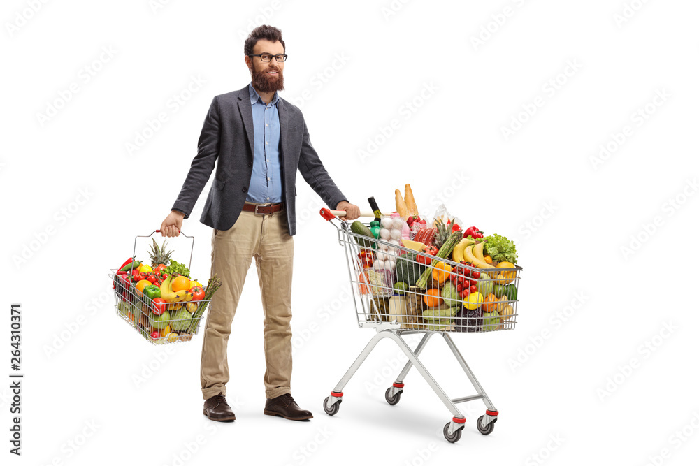 Wall mural young man standing with a shopping cart and a shopping basket with fruits and vegetables