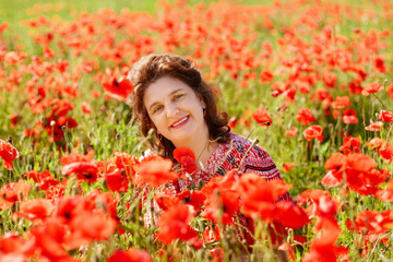 Naklejka premium Portrait smiling happy old Elderly woman having fun, walking in a field with poppy flowers. Healthcare lifestyle senior lady relax in spring. Female in summer time.