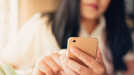 Close up of young woman sitting at cafe with mobile phone. using smart phone at coffee shop. Blurred background and Soft focus.