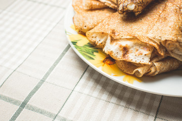 Delicious pancakes cooked in pan lie in small saucer on kitchen table.