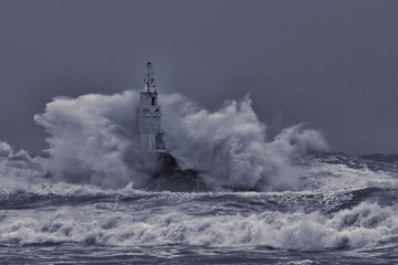 Old lighthouse in the middle of great stormy waves.Crashing big sea wave against rocks splash and spray .Huge stormy sea wave splash