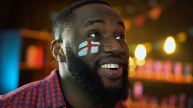 Joyful black soccer fan with english flag painted on cheek celebrating victory