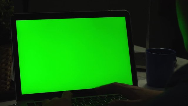 Over the shoulder shot of a young boy using on laptop computer on desk, looking at green screen. Dolly shoot 60fps.