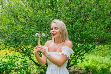 Beautiful blonde woman blowing on white blowball
