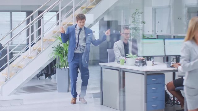 Young Fun Loving and Handsome Businessman Dances Through the Open Space Office Hallway. Worker Celebrating his Latest Achievement. Diverse and Motivated Business People Work on Desktop Computers