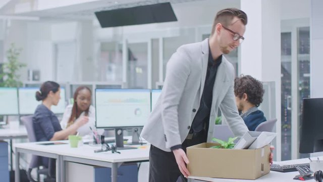 Sad Fired / Let Go Office Worker Packs His Belongings into Cardboard Box and Leaves Office. Workforce Reduction, Downsizing, Reorganization, Restructuring, Outsourcing. Mass Unemployment Market Crisis