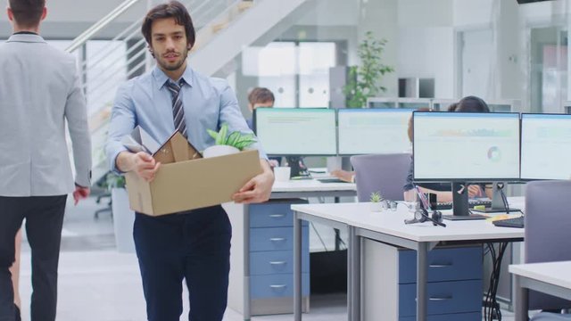 Sad Fired / Let Go Office Worker Packs His Belongings into Cardboard Box and Leaves Office. Workforce Reduction, Downsizing, Reorganization, Restructuring, Outsourcing. Mass Unemployment Market Crisis