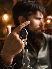 Man with beard holds glass brandy. Macho drinking. Confident man with car keys in his hand. Do not drink and drive Cropped image of drunk man talking car keys.