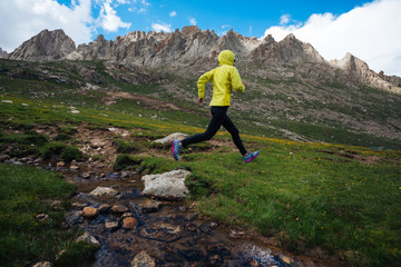 Woman trail runner jumping over small river on beautiful mountains