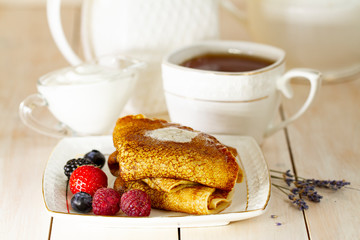 Delicious thin pancakes close up, with fresh blueberries and cream on white wooden background. Sweet Homemade Stack of Pancakes with Butter, fresh forest berries and cream or yogurt with lavender tea