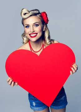 smiling woman holding heart symbol, dressed in pin-up style