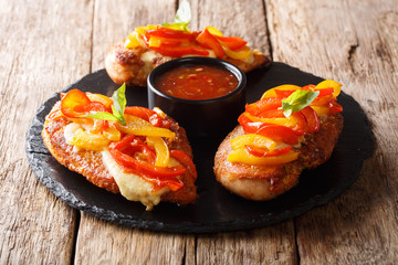 Delicious baked chicken breast with parmesan cheese and bell peppers, served with sauce close-up on a table. horizontal