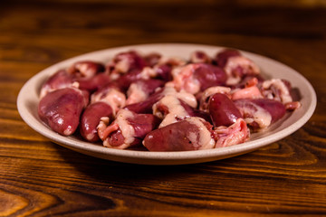 Ceramic plate with raw chicken hearts on wooden table