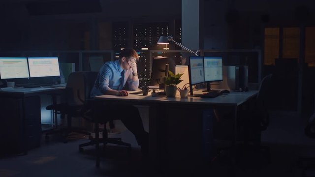 In the Office at Night, Overworked Tired Office Worker Uses Desktop Computer but Falls Asleep Fast. Tired Frustrated Exhausted Businessman Falls asleep at His Job