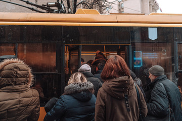 Many unidentified people are waiting for city transport at the bus stop