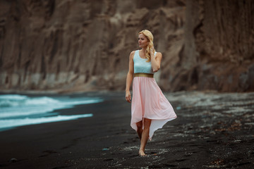 blond woman on a black beach on Santorini, with cliff in the background and a rough sea