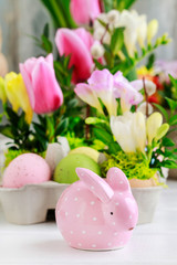 Pink ceramic rabbit in front od easter table floral decoration.