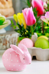 Pink ceramic rabbit in front od easter table floral decoration.