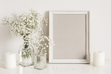 Candles, gypsophila flowers and photo frame on table wall background. Front view mockup