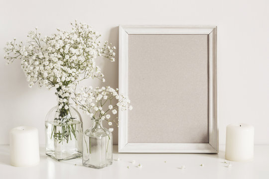 Candles, gypsophila flowers and photo frame on table wall background. Front view mockup © colnihko